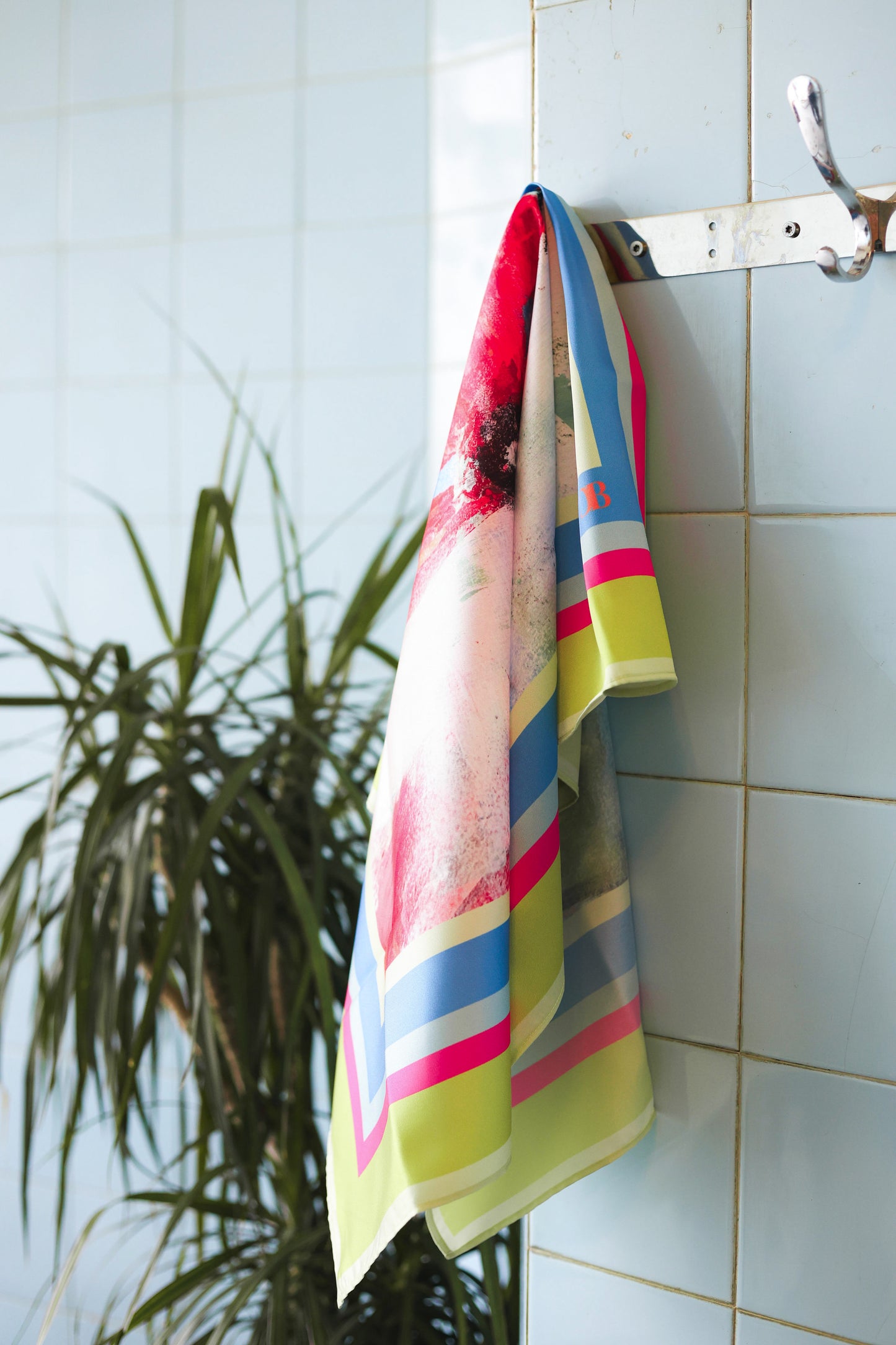 Colorful scarf hanging on a tiled wall with a plant in the background