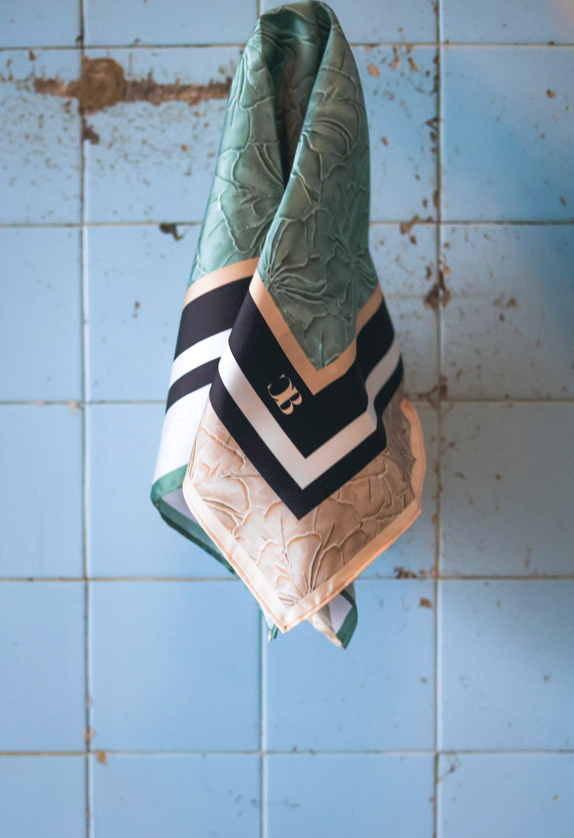 Green and beige scarf with a logo on a blue tiled wall
